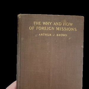 Pode incluir: Um livro castanho com o título "The Why and How of Foreign Missions" de Arthur J. Brown.