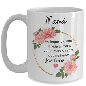 May include: White ceramic coffee mug with a black floral design and the text "Mam&aacute; no importa c&oacute;mo la vida te trate, por lo menos sabes que no tienes hijos feos".