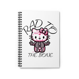 May include: A white spiral notebook featuring a pink and black illustration of a Hello Kitty character with a skeleton inside. The text "RAD TO THE BONE" is written in black above the character.