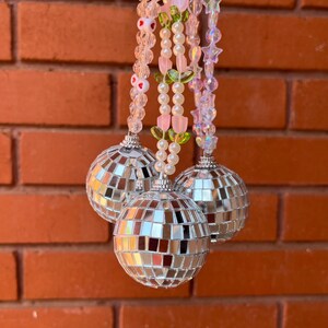 May include: Three silver disco ball ornaments hanging from a beaded chain with pink, green, and white beads.