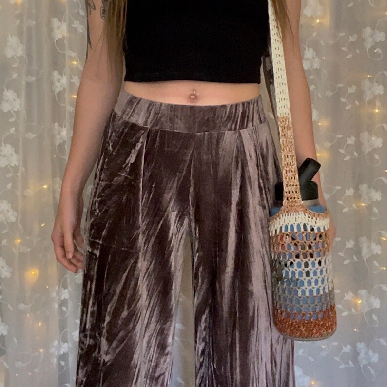 May include: A person wearing a brown velvet pants with a crocheted bag with a water bottle inside.