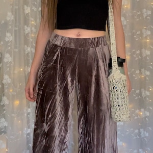 May include: A person wearing a pair of wide-leg, mauve velvet pants with a crocheted bag.