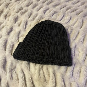 May include: A black knitted beanie hat with a ribbed texture. The hat is made of a soft, warm material and is perfect for cold weather.