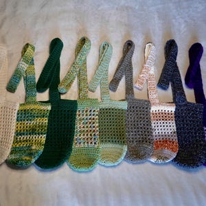 May include: Ten crocheted bags with different colored stripes and patterns. The bags have long straps and are made of a soft, textured yarn.
