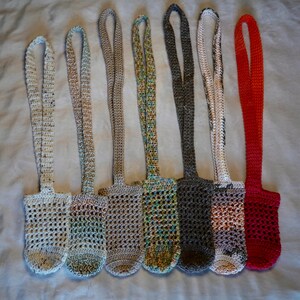 May include: Seven crocheted bottle holders in various colors, including white, beige, green, gray, and red. The holders are made with a simple, open stitch pattern and have long straps for carrying.