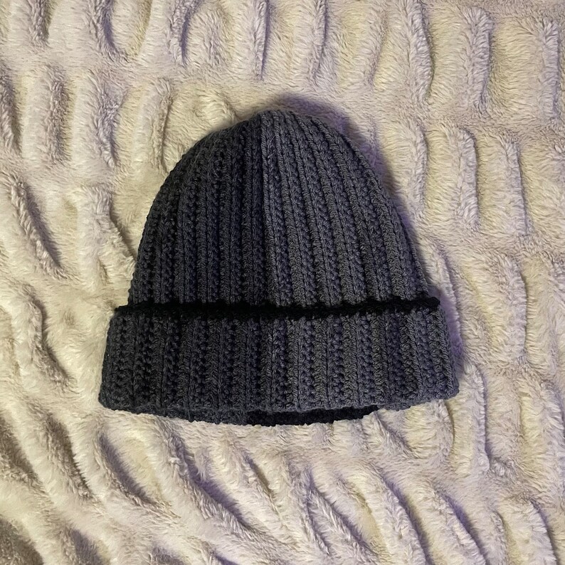 May include: A dark gray knitted beanie with a black trim. The beanie is made of a soft, warm material and has a ribbed texture.