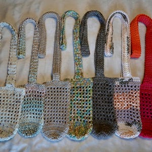 May include: Seven crocheted bottle holders with different colored yarn. The holders are made with a simple stitch pattern and have a long strap for carrying.
