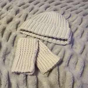 May include: A white crocheted beanie and matching wrist warmers. The beanie has a ribbed texture and the wrist warmers have a simple stitch pattern.