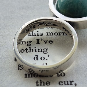 May include: Close-up of two silver rings. One ring is in focus, displaying the text "925S" and other markings. The second ring holds a green, spherical stone. The rings are on a page with printed text.