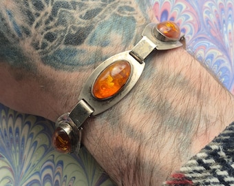 Puede incluir: Un brazalete de plata con tres piedras de ámbar ovaladas. El brazalete está en la muñeca de una persona.