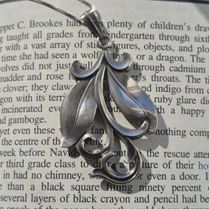 May include: A silver pendant necklace featuring a floral design. The pendant is shaped like three leaves, with a delicate chain.