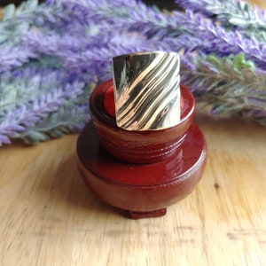 May include: A silver ring with a textured, wavy design. The ring is displayed on a red ring holder.