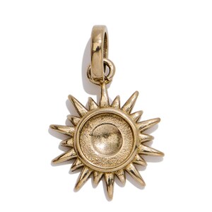May include: A gold-toned metal pendant shaped like a sun with a central circular disc and radiating pointed rays. The pendant features a textured finish on the inner circle and includes a small attached jump ring at the top for suspension.
