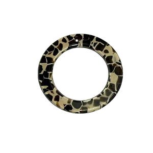 May include: A circular ring with a mosaic pattern of black, tan, and cream-colored shapes. The ring is made of a glossy material and has a smooth, rounded edge. The design is reminiscent of animal print.