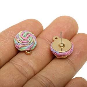 May include: A pair of pastel-coloured woven stud earrings. Each earring has a circular design with a gold-coloured post and backing. The woven pattern incorporates shades of pink, green, and yellow, creating a delicate and colourful accessory.