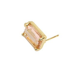 May include: A single gold-colored stud earring with a rectangular, peach-colored gemstone. The earring has a post for insertion and is set against a white background. The gemstone is faceted.