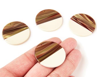 May include: Four round, two-tone pendants. The top half of each pendant features a swirling pattern of brown, gold, and cream colors, while the bottom half is solid cream. Each pendant has a small hole at the top for stringing.