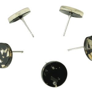 Puede incluir: Cinco pendientes de botón negros con postes plateados. Los pendientes tienen un diseño redondo y plano con una base negra y escamas metálicas plateadas y doradas incrustadas. Los postes son plateados.