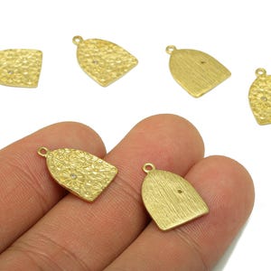 May include: Gold-coloured bell-shaped charms with textured surfaces and small loops for attaching to jewellery. Some charms have floral patterns or small crystals. The charms are displayed against a white background.