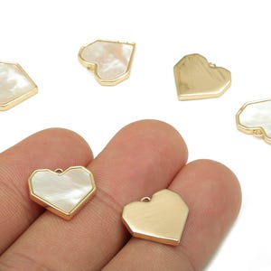 May include: Heart-shaped pendants with a gold-colored border and a pearlescent white center. Some pendants are solid gold. These jewelry findings are ideal for crafting earrings, necklaces, or other accessories.
