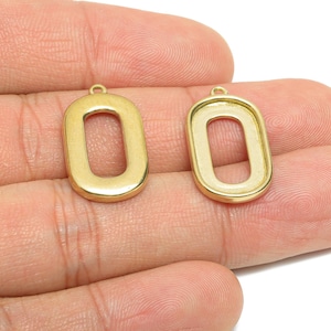 May include: Two gold-colored, open-center, rectangular pendants. Each pendant has a small loop at the top for attaching to a chain or other jewelry component. The pendants are shown against a neutral background.