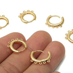 May include: Gold-coloured hoop earrings with a distinctive design. Each earring has a series of small, decorative loops along the bottom edge. The earrings are shown in a close-up view, highlighting their shiny, metallic finish. These earrings are a stylish accessory.