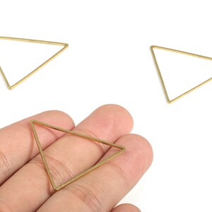 May include: Three gold triangle shaped metal hoops. One hoop is being held in a hand.