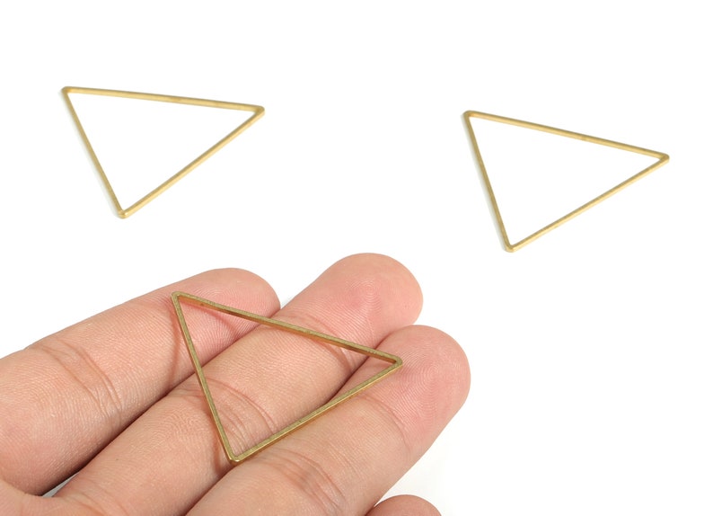 May include: Three gold triangle shaped metal hoops. One hoop is being held in a hand.