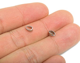 May include: Two small, silver-colored jewelry bails are displayed on a person's hand. The bails are oval-shaped with a small loop for attaching to a pendant or other jewelry component. The bails are made of a shiny metal.