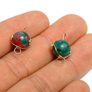 May include: Two gemstone pendants with gold wire wrapping. One pendant is a mix of red and green, the other is solid green. Each has a small loop at the top and bottom for attaching to a chain or earring hook.