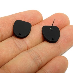 May include: A pair of matte black stud earrings. Each earring has a rounded, asymmetrical shape with a small hole near the bottom. One earring has a silver post for piercing. Jewellery.