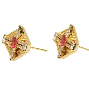 以下が含まれることがあります： 幾何学模様のゴールドのイヤリングのペア。各イヤリングは、中心にピンクとクリアなクリスタルがセットされ、周囲を小さなクリアなクリスタルが囲んでいます。