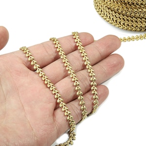 May include: Gold chain trim with a leaf design. The chain is shown in a hand, with the chain coiled up in the background.