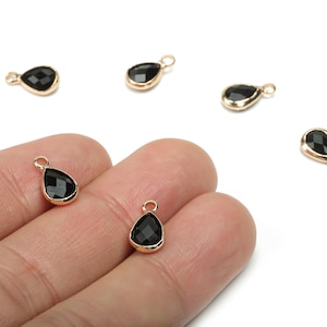 May include: Black teardrop charms with gold-coloured metal edging. Each charm has a small loop at the top for attaching to jewellery. The faceted black stones catch the light, creating a sparkling effect. These charms are ideal for jewellery making.