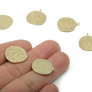 Könnte beinhalten: Goldfarbene Metallanhänger in verschiedenen Formen, darunter rund und unregelmäßig, mit strukturierter Oberfläche. Einige Anhänger weisen ein Sonnenmuster auf. Die Anhänger haben kleine Schlaufen zum Befestigen an Schmuck.