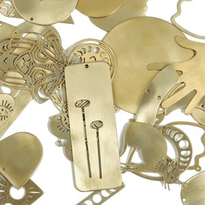 May include: A collection of gold-toned metal charms with various designs, including a heart, a butterfly, a hand, and a cat. The charms are cut out and have a delicate, intricate design.