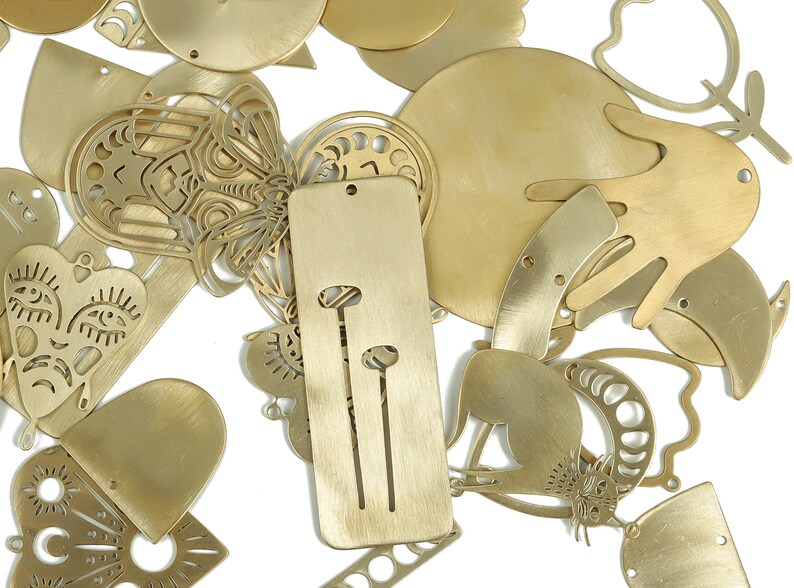 May include: A collection of gold-toned metal charms with various designs, including a heart, a butterfly, a hand, and a cat. The charms are cut out and have a delicate, intricate design.