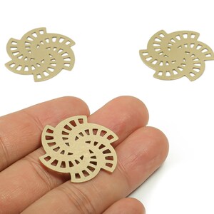 May include: Three gold-colored metal charms in a floral design. One charm is held in a hand, while two others are placed on a white surface. The charms have a cut-out pattern.