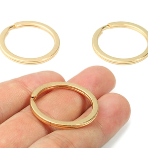 Peut inclure: Trois porte-clés dorés. Un porte-clés est tenu dans une main. Les porte-clés sont ronds avec une fente pour attacher les clés. Les porte-clés ont un design à double couche.