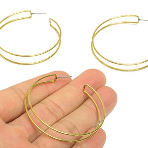 Peut inclure: Trois boucles d'oreilles créoles dorées. Chaque boucle d'oreille présente un design à double couche. Les boucles d'oreilles sont présentées sur fond blanc. Les boucles d'oreilles mesurent environ 5 cm de diamètre.