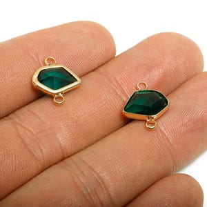 Peut inclure: Deux connecteurs de pierres précieuses vert émeraude avec des montures en métal doré. Chaque connecteur a une forme géométrique unique avec une boucle en haut et en bas pour la fixation. Les pierres sont facettées.