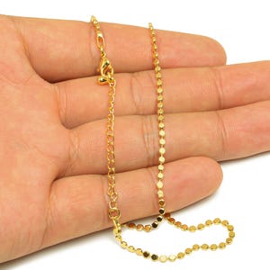 Könnte beinhalten: Eine goldene Kettenkette mit einem zarten, runden Gliederdesign. Die Kette wird auf einer Hand gezeigt, wobei der Verschluss sichtbar ist.