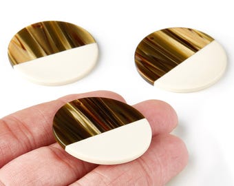 May include: Three round, two-toned beads. The top half of each bead is a mix of brown and gold tones, while the bottom half is a solid cream color. One bead is held in a hand, and two are on a white surface.