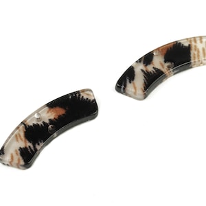 Może przedstawiać: Dwa spinki do włosów w czarno-brązowo-biały wzór. Spinki są zakrzywione i mają błyszczące wykończenie.