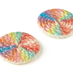 Puede incluir: Dos botones redondos tejidos con un patrón de arcoíris. Los botones están hechos de un material blanco y tienen un diseño tejido con un arcoíris de colores.