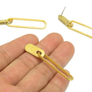 Könnte beinhalten: Goldfarbene, längliche Kettenglieder-Ohrringe. Die Ohrringe haben ein rechteckiges Oberteil mit einem Stecker und ein langes, oval geformtes Unterteil. Das Design ist schlicht und modern, geeignet für den Alltag oder besondere Anlässe.