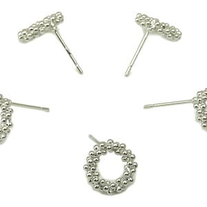 Puede incluir: Un juego de cuatro pendientes de botón plateados. Dos pendientes presentan un diseño circular hecho de pequeñas cuentas, mientras que los otros dos pendientes son una simple línea recta de cuentas.