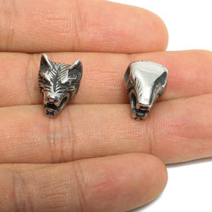 May include: Two silver metal beads shaped like animal heads. One is a detailed wolf head, the other a bear head. The small beads have holes for threading. Ideal for jewellery making.