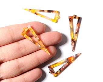 Puede incluir: Cuatro colgantes triangulares calados con un patrón de carey amarillo, naranja y marrón. Los colgantes se muestran sobre un fondo blanco, uno de ellos apoyado en una mano.