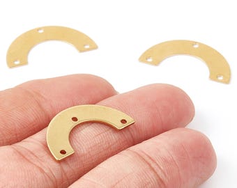 Puede incluir: Primer plano de varios hallazgos de joyería dorados en forma de media luna. Cada hallazgo tiene tres pequeños agujeros para sujetar a otros componentes. Los hallazgos se muestran sobre un fondo blanco, uno de ellos sostenido en una mano.